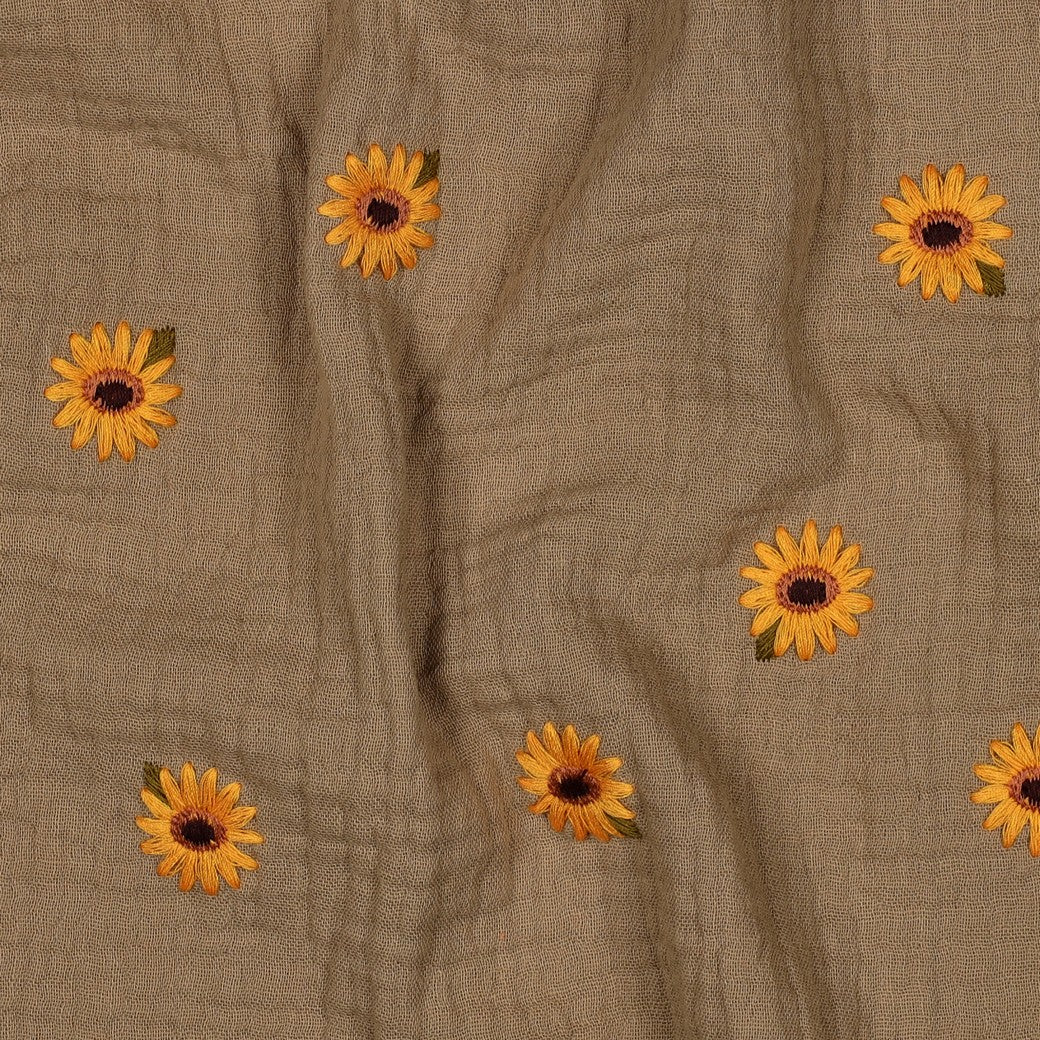 Detailaufnahme des sandfsrbenen Musselinstoffes mit den gestickten Sonnenblumen